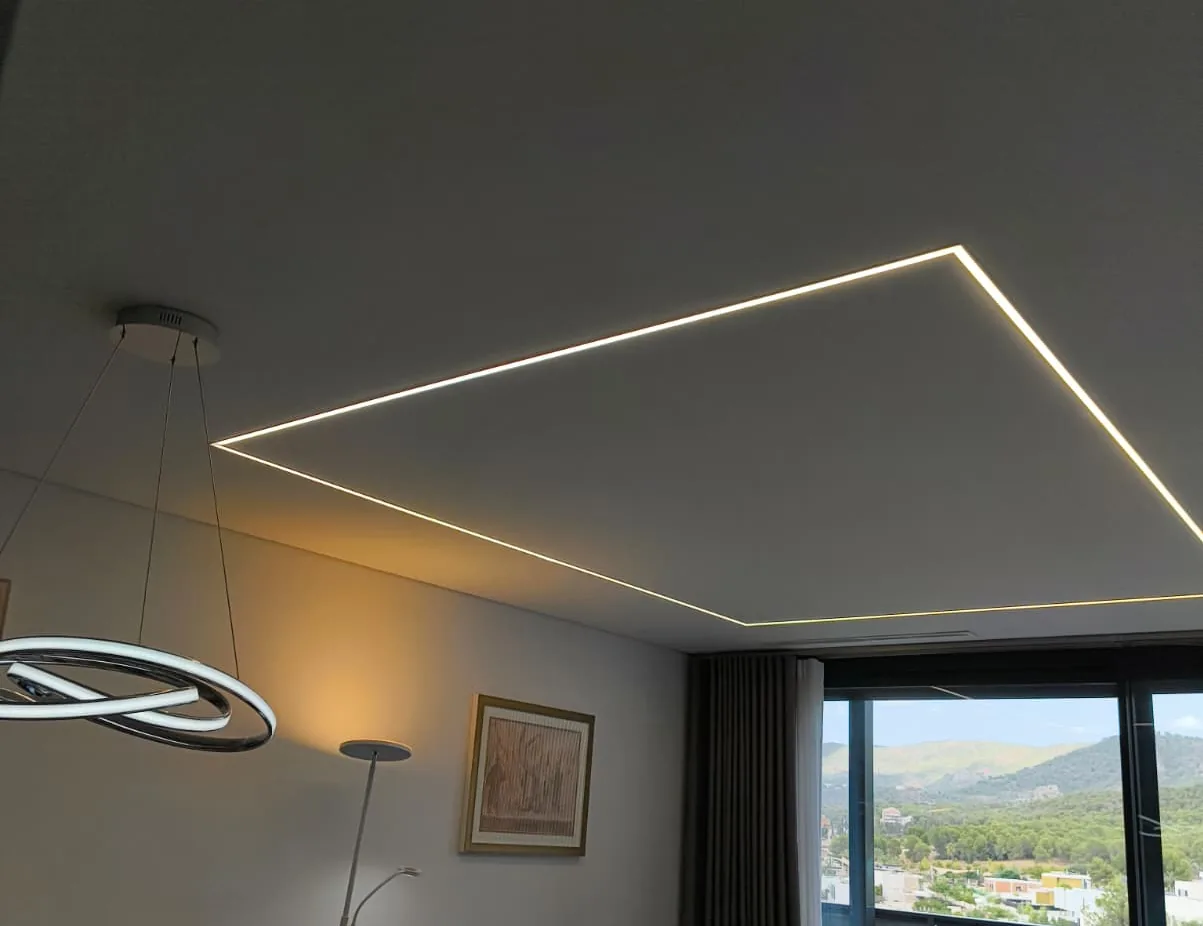 Perímetro de luz lineal encendido en el techo de un salón, con lámpara circular colgante